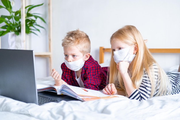 Nauka Na Odległość Edukacja Online Choroba Chłopiec I Dziewczynka W Masce Medycznej Studiuje W Domu Z Cyfrowym Tabletem Laptop Notebook I Odrabia Pracę Domową Siedzi Na łóżku Z Książkami Szkoleniowymi