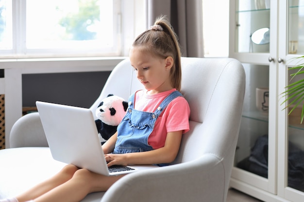 Nauka na odległość. Wesoła dziewczynka przy użyciu komputera przenośnego studiując za pośrednictwem systemu e-learningu online.