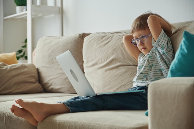 Nauka w domu nauka na odległość Dziecko korzystające z laptopa siedząc na kanapie w domu