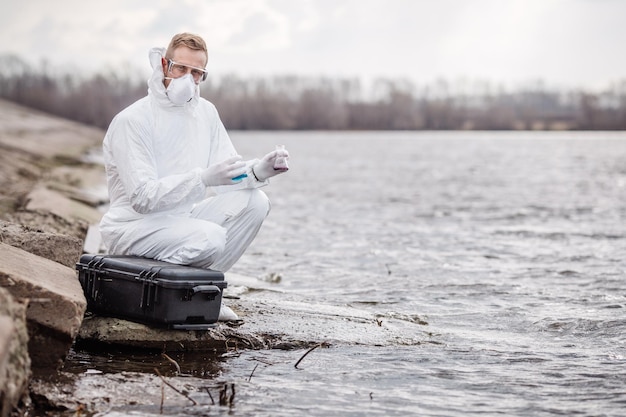 Naukowiec lub biolog w mundurze ochronnym badający płynną zawartość probówki xA