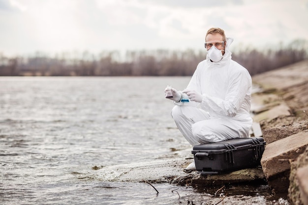 Naukowiec lub biolog w mundurze ochronnym badający płynną zawartość probówki xA