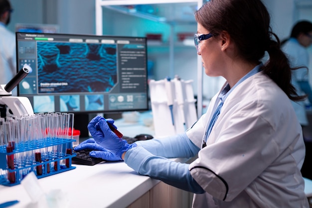 Naukowiec piszący na laptopie trzymający chemię opieki zdrowotnej vacutainer krwi