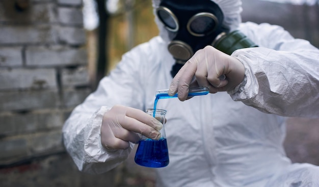 Zdjęcie naukowiec prowadzący badania na zewnątrz w białym kombinezonie i masce przeciwgazowej