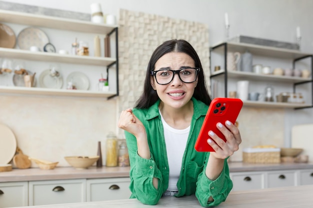 Nerwowa młoda kobieta w okularach trzymająca czerwony telefon i czekająca na ważny telefon lub