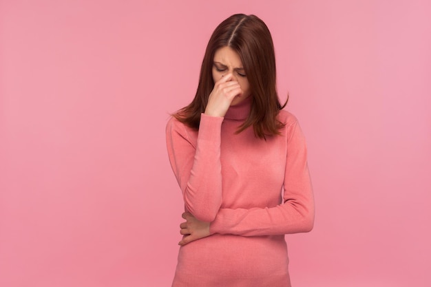 Nerwowo przygnębiona brunetka w różowym swetrze płacze chowając oczy w dłoni, czuje się zdesperowana z powodu zerwania lub rozwodu. Kryty strzał studio na białym tle na różowym tle