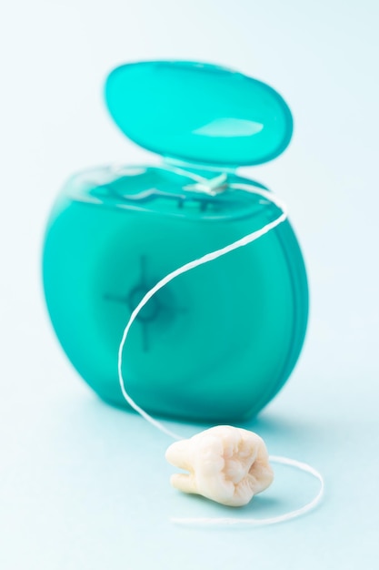 Zdjęcie nić dentystyczna i prawdziwy ząb na niebieskim tle zapobieganie pielęgnacji pomaga oszczędzać zęby z bliska