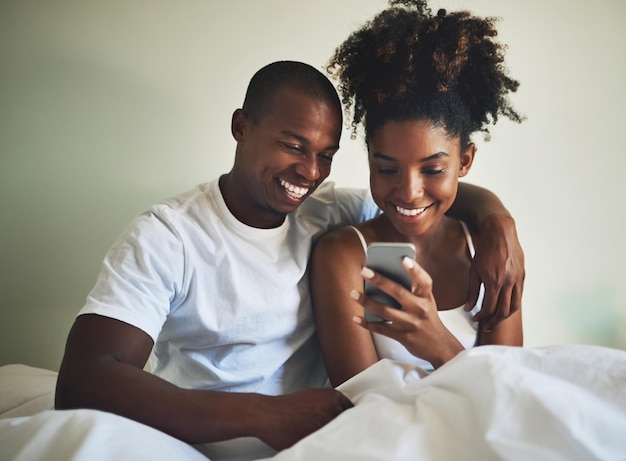 Nic tak nie mówi o miłości jak wspólne konto w mediach społecznościowych Ujęcie szczęśliwej młodej pary korzystającej z telefonu komórkowego w łóżku w domu