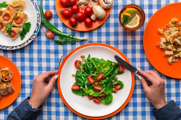 Nie do poznania kobieta jedzenie świeżej sałatki z zieleniną i pomidorami na tle obrus w kratkę. Zdrowe odżywianie koncepcja, widok z góry organicznych warzyw.