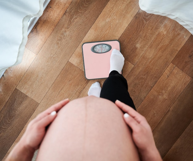Nie do poznania kobieta w ciąży z dużym brzuchem patrząca w dół podczas sprawdzania wagi na wadze elektronicznej przycięta matka z brzuchem martwiąca się o figurę podczas macierzyńskiego nastroju
