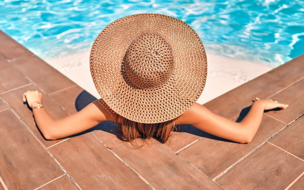 Nie do poznania kobieta w wielkim kapeluszu relaksuje się na basenie Widok z tyłu