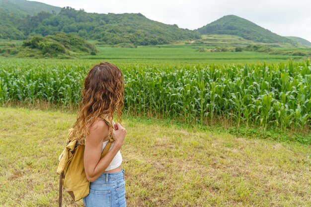 Nie do poznania kobieta wędrująca po polu kukurydzy. Poziomy widok podróżnika z plecakiem w górach.