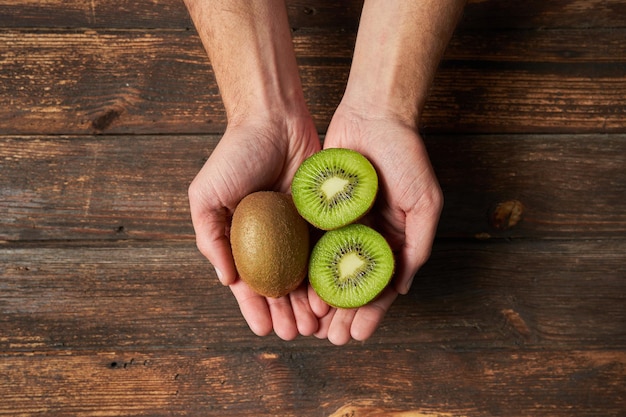 Nie do poznania mężczyzna pokazujący rękami dojrzałe owoce kiwi i pół kiwi na drewnianym tle