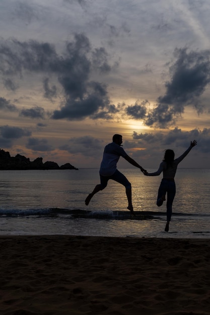 Nie do poznania zakochana para skacząca szczęśliwie na brzegu plaży o zachodzie słońca