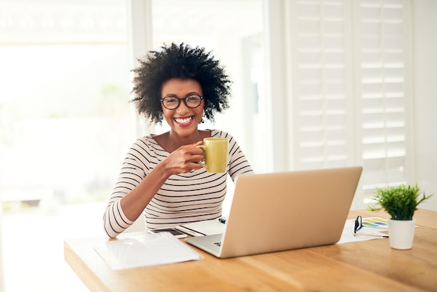 Nie ma to jak filiżanka komfortu na rozpoczęcie dnia Portret młodej kobiety pijącej kawę podczas pracy na laptopie w domu