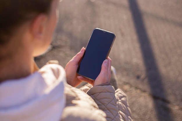 Nie widać twarzy młodej kobiety trzymającej telefon na ulicy