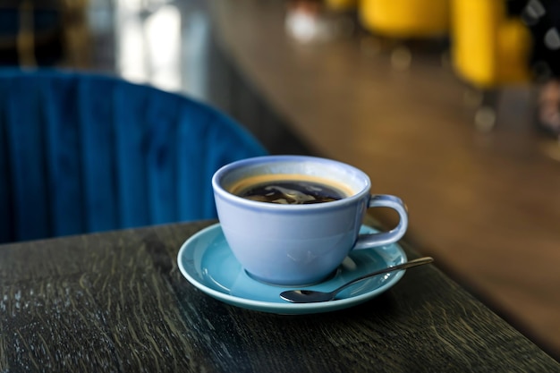 Niebieska ceramiczna filiżanka gorącej czarnej kawy z bliska na drewnianym stole w atmosferze kawiarnianej przestrzeni