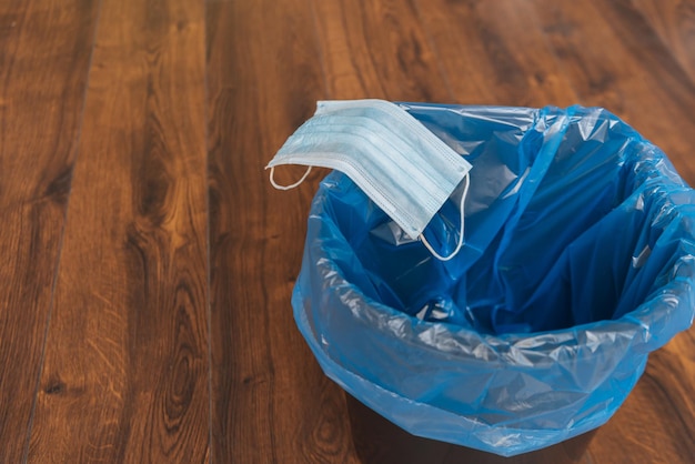 Niebieska maska medyczna w koszu na śmieci z workiem na śmieci na końcu koncepcji kwarantanny