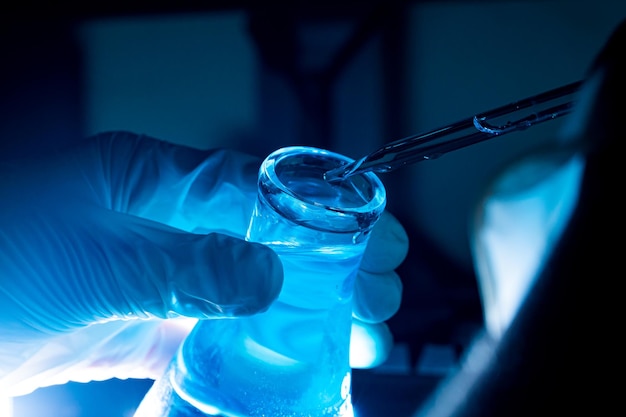 niebieska szklana probówka, azjatycka kobieta naukowiec z probówkami przeprowadzająca badania w laboratoriach klinicznych