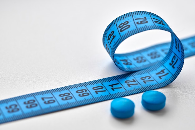 Niebieska taśma centymetrowa i okrągłe tabletki odchudzające na białym tle. Dieta, odchudzanie i koncepcja odchudzania.