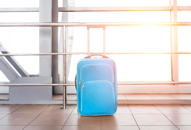 Niebieska walizka w budynku lotniska przed oknem z rozbłyskiem słonecznym