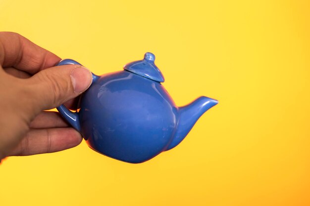 Niebieski ceramiczny czajniczek do robienia herbaty w dłoni na żółtym tle