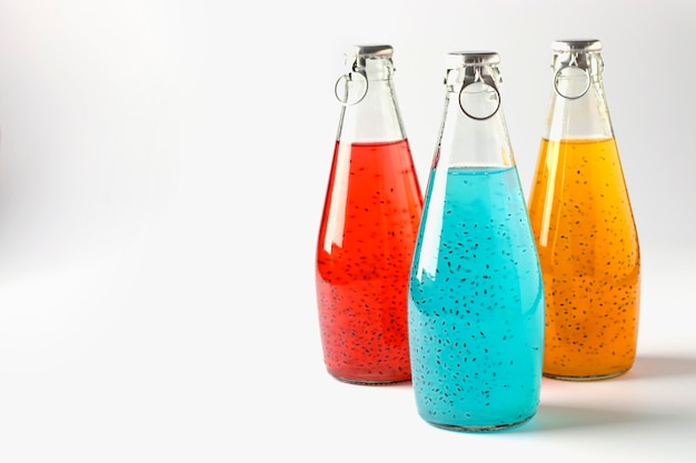 Zdjęcie niebieski, czerwony i pomarańczowy napoje z nasionami bazylii w butelkach na białej powierzchni, zbliżenie, kopia przestrzeń