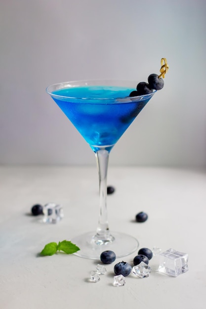 Niebieski koktajl w szklance martini z miętą w kostkach lodu i jagodami