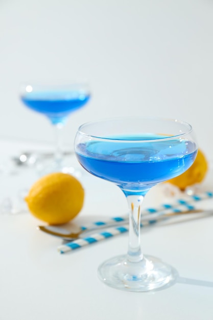 Niebieski koktajl w szkle, całe słomki z cytryny i kostki lodu na białym tle.
