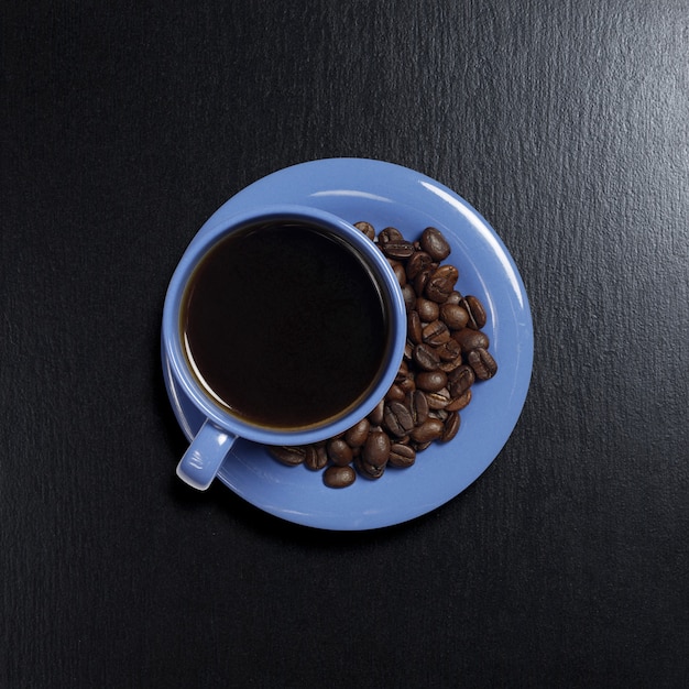 Niebieski kubek kawy i ziaren na czarnym tle kamienia