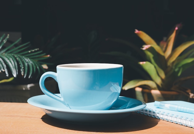 Niebieski kubek kawy z notatnikiem i długopisem na drewnianym stole w ogrodzie