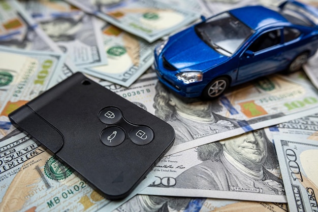 Niebieski mały samochodzik z prawdziwymi kluczykami do samochodu leżącymi w gotówce w dolarach