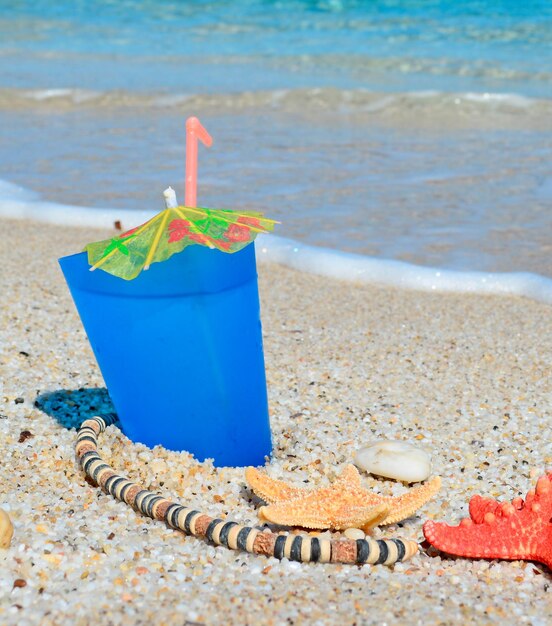 Niebieski napój z muszlami i naszyjnikiem przy brzegu