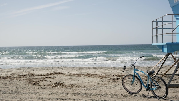 Niebieski rower, rower typu cruiser na plaży morskiej oceanu, wybrzeże Kalifornii USA. Jedź obok wieży ratowniczej.