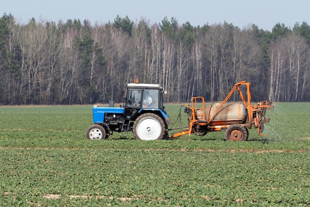 Niebieski traktor rozpylający pestycydy na polu z opryskiwaczem Maszyny rolnicze pracują w terenie Chemiczne pestycydy są skutecznymi narzędziami do ochrony darni i roślin