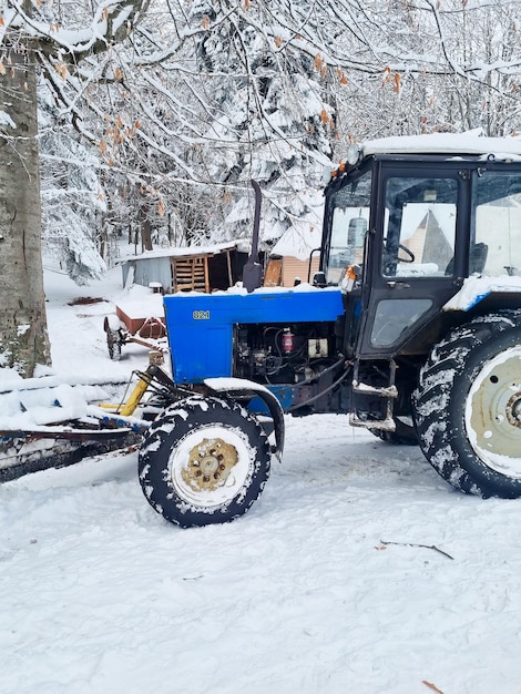 Niebieski traktor z dużymi kołami w śnieżnym lesie