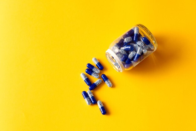 Zdjęcie niebieskie kapsułki witaminowe wylewane z słoika na żółtym tle