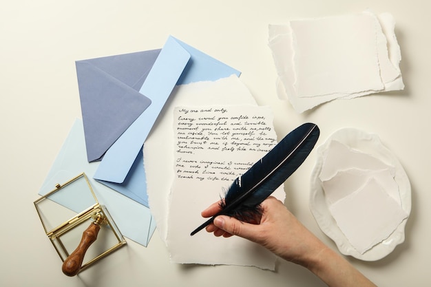 Niebieskie koperty prześcieradła papierowego piórka w dłoni i listu z tekstem na białym tle widok z góry