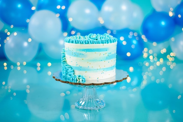 Niebiesko-biały tort urodzinowy z balonami w tle. Dekoracja zestawu fotograficznego do sesji zdjęciowej.