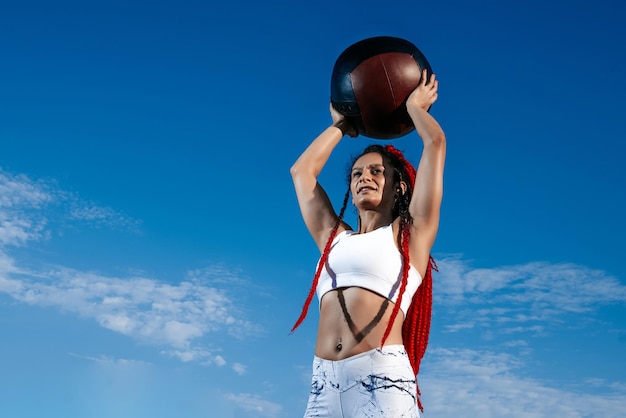 Niebo w tle Wysportowana kobieta z piłką lekarską Siła i motywacja Zdjęcie wysportowanej kobiety w modnej odzieży sportowej