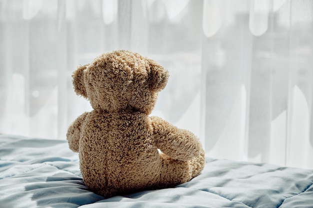 Zdjęcie niedźwiadkowa lalka siedzi z powrotem na łóżku