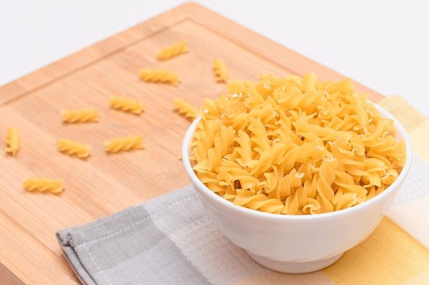 Niegotowany makaron fusilli w białej misce na drewnianej desce