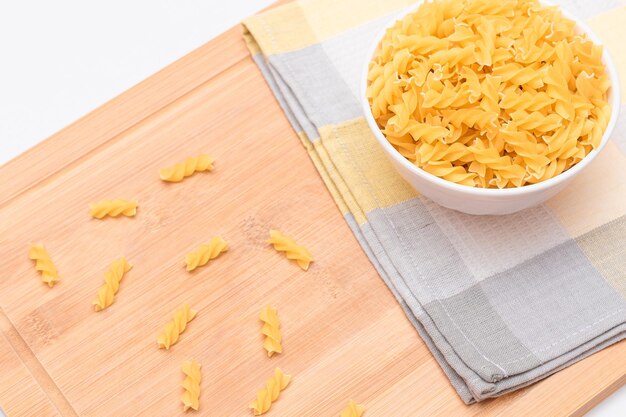 Niegotowany makaron fusilli w białej misce na drewnianej desce