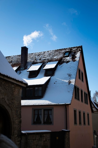 Niemiecki dom z dachem pokrytym śniegiem i kominem wypluwającym dym na niebieskim niebie