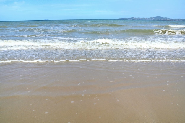 Nieostre fale biją na plaży z piaskiem i błękitne niebo z odbiciem w letni poranek.