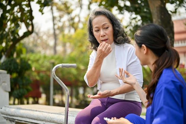Niepełnosprawna Azjatka w wieku 60 lat bierze tabletkę leku podczas odpoczynku na ławce w parku