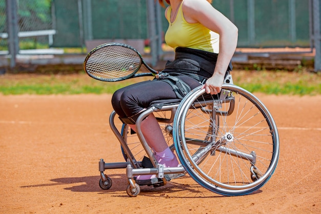 Zdjęcie niepełnosprawna młoda kobieta bawić się tenisa na tenisowym korcie na wózku inwalidzkim.