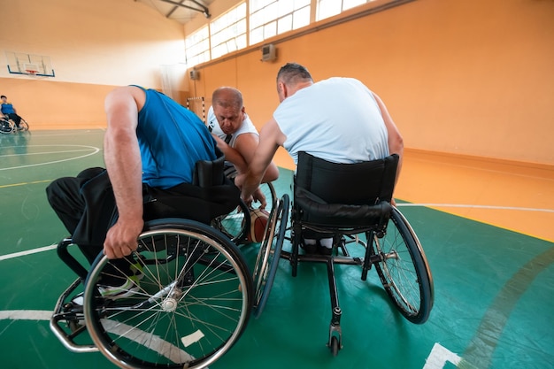 Niepełnosprawni weterani wojenni lub pracy mieszani ras i wiekowych drużyn koszykówki na wózkach inwalidzkich rozgrywający mecz treningowy w hali sportowej siłowni. Koncepcja rehabilitacji i integracji osób niepełnosprawnych. Wysokiej jakości zdjęcie