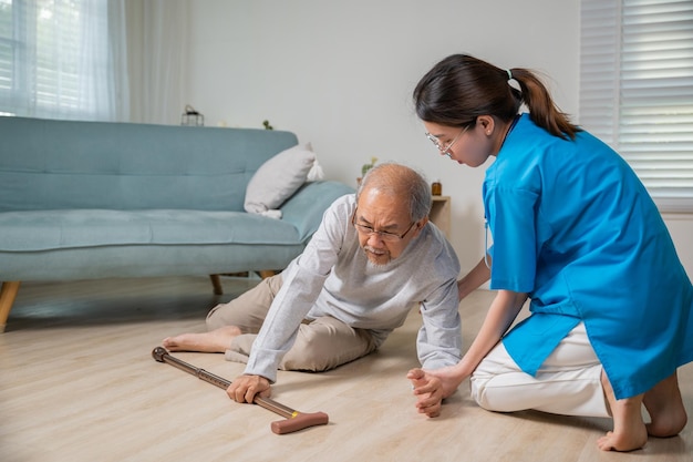 Niepełnosprawny starszy pacjent z laską spada na podłogę i troskliwy młody asystent