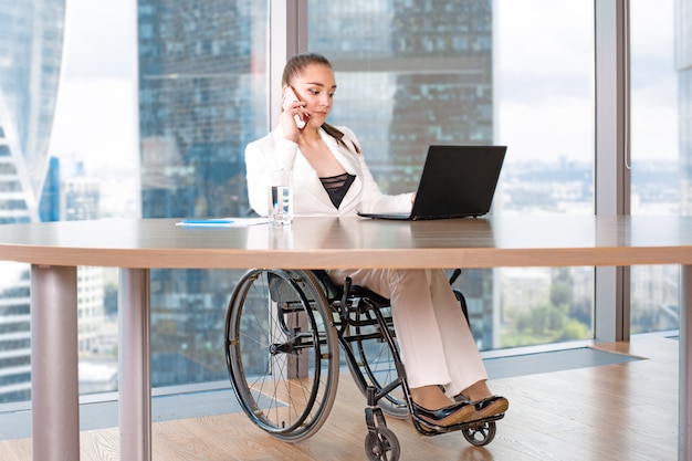 Nieprawidłowy lub niepełnosprawny młody biznes kobieta siedzi wózek inwalidzki pracujący w biurze na laptopie