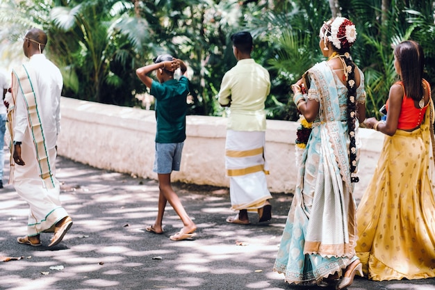 Nierozpoznani mieszkańcy w tradycyjnych strojach przechadzają się po Parku na wyspie Mauritius, Tradycyjne suknie ślubne na Mauritiusie.